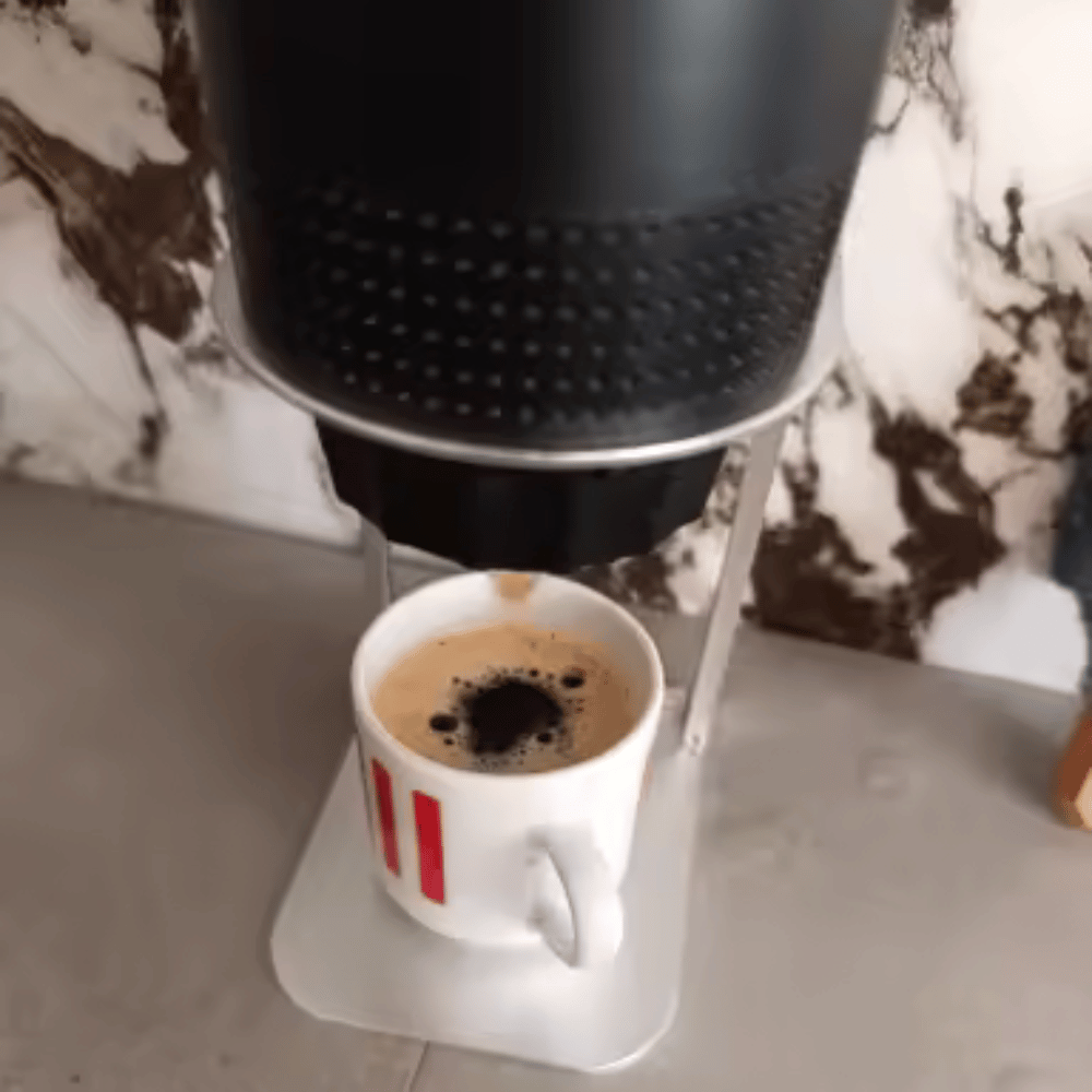 Coffee being dispensed into a white cup with red stripes from a black coffee machine on a marble surface.