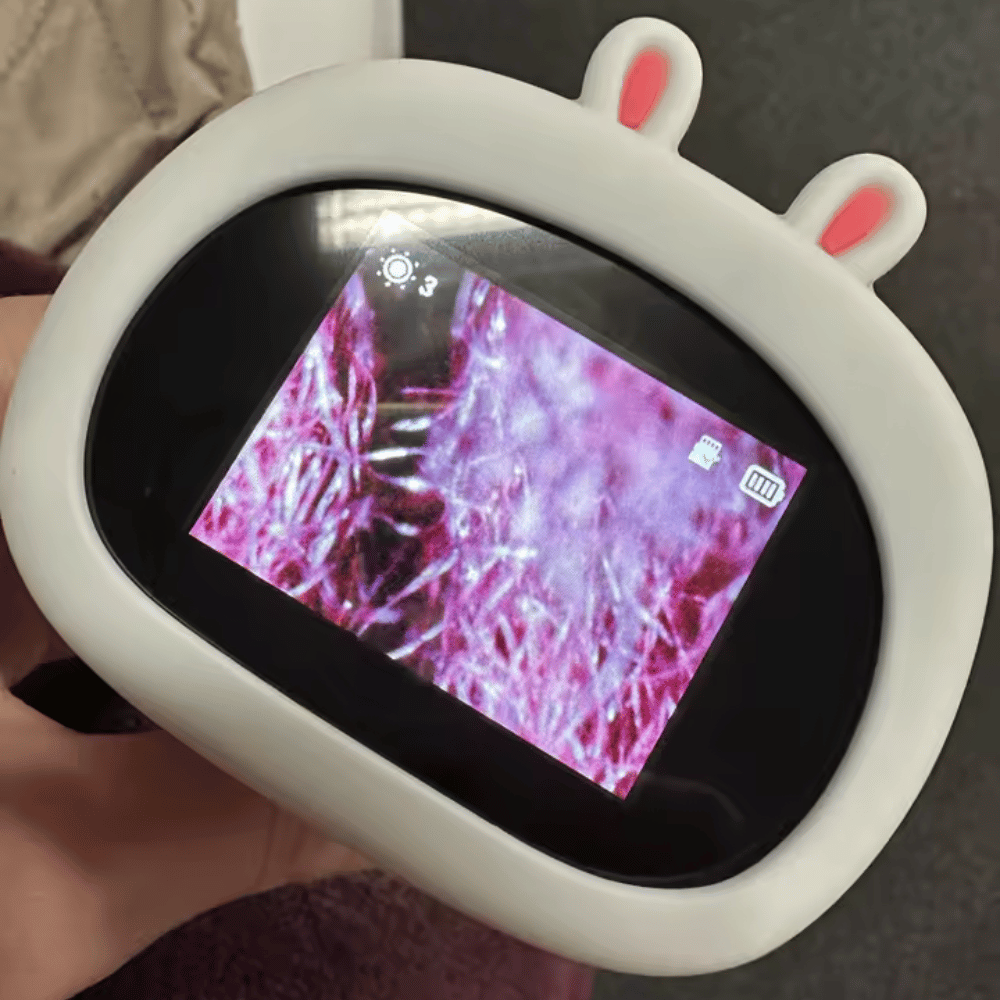 Small electronic device with a screen displaying a pinkish texture, held by a hand.