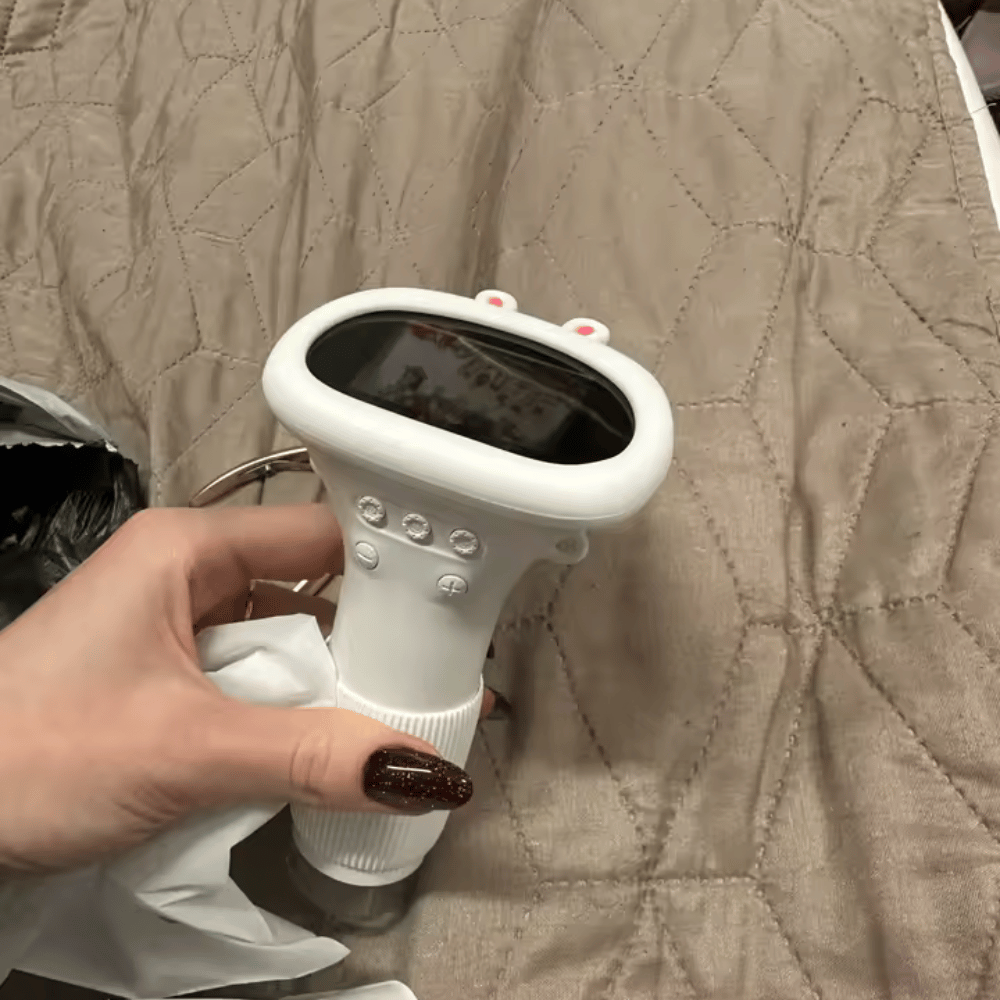 Hand holding a white electronic device with a screen on a beige quilted surface