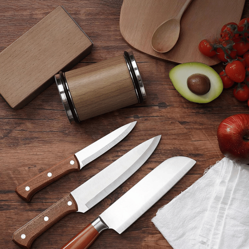Three kitchen knives with wooden handles on a wooden surface with fruits and a cutting board.